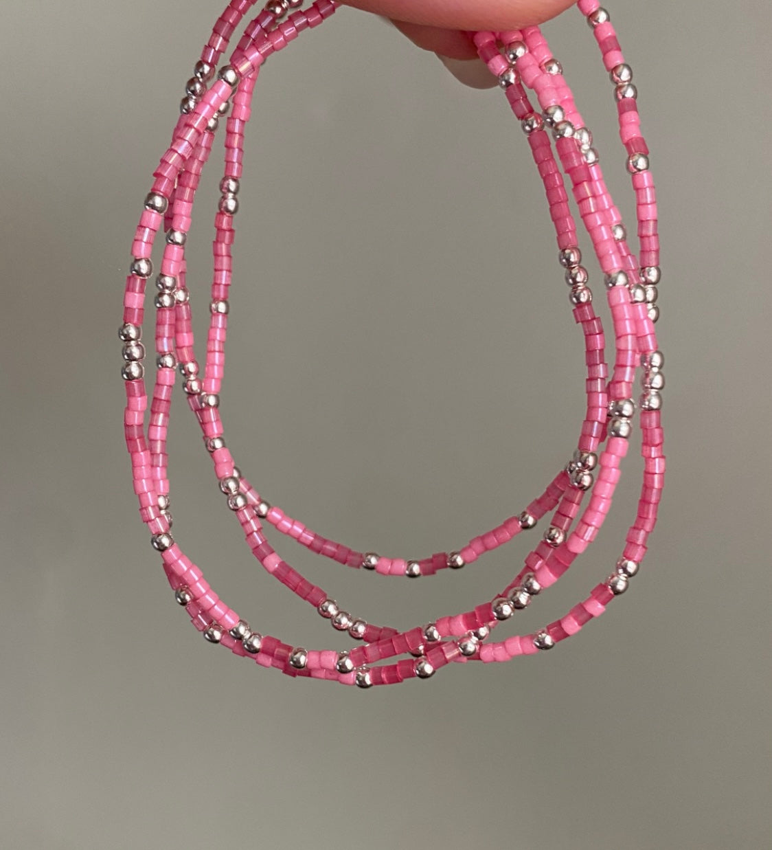 Pink beaded necklace with silver accents held against a neutral background