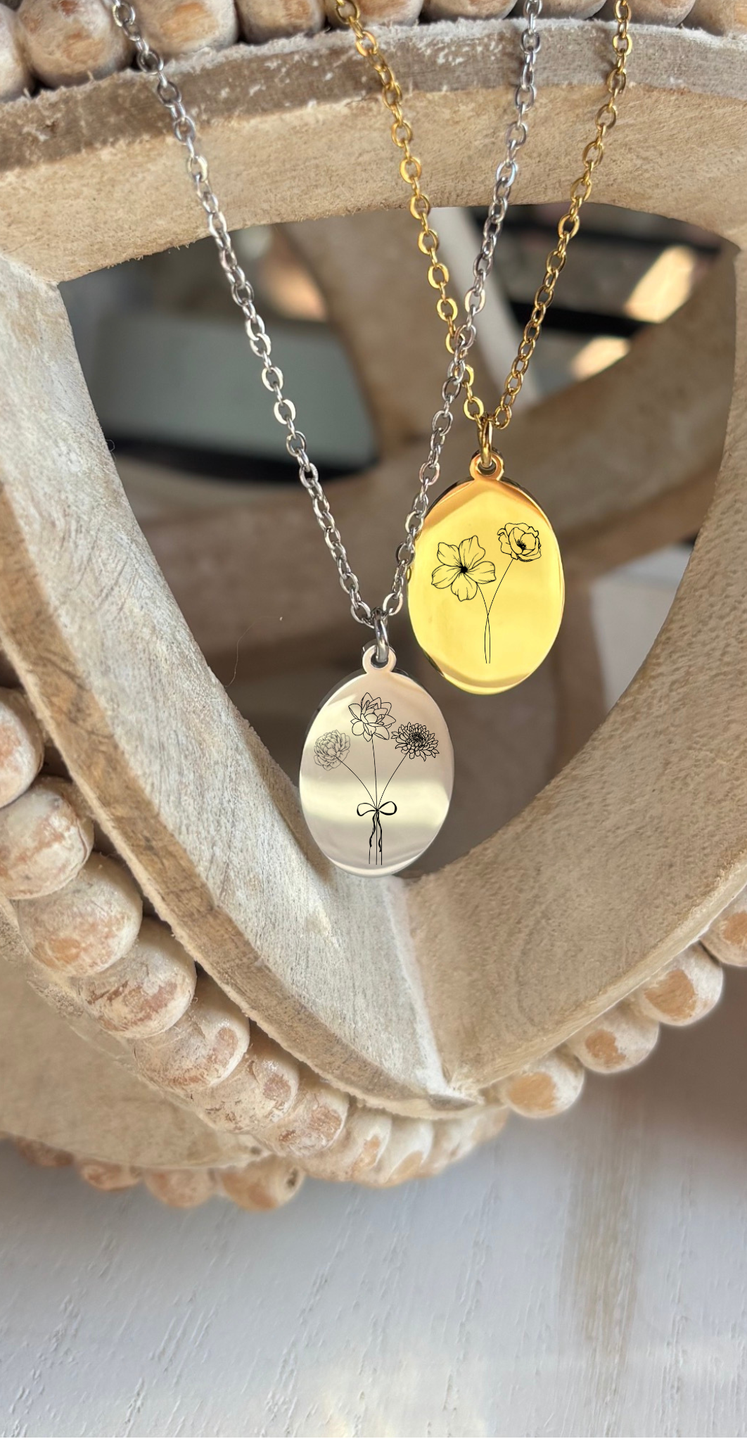 Two gold necklaces with engraved pendants on a wooden stand.