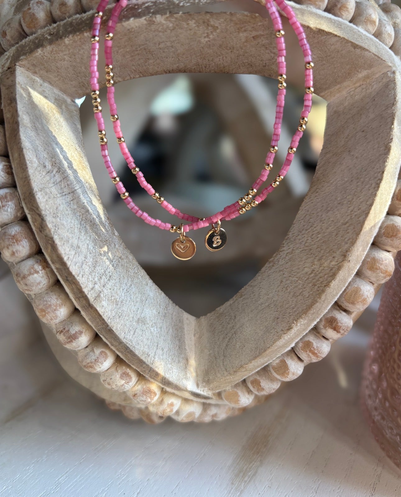 Pink beaded bracelets with gold accents on a wooden heart-shaped display