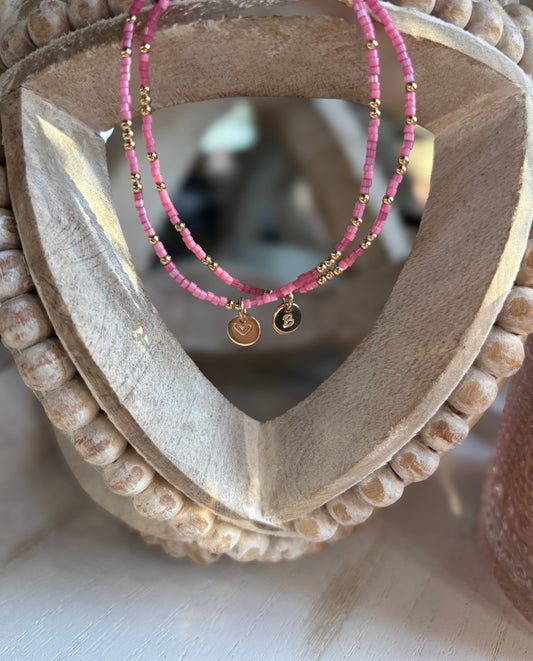 Pink beaded bracelets with gold accents on a wooden heart-shaped display