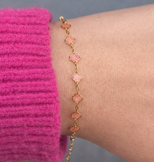 Gold bracelet witch pink stones on a wrist against a pink sleeve.
