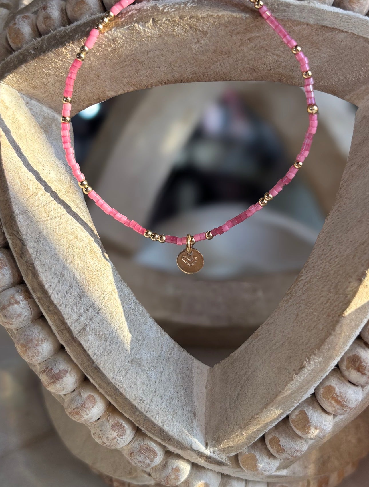 Pink beaded bracelet with gold accents on a decorative stone surface