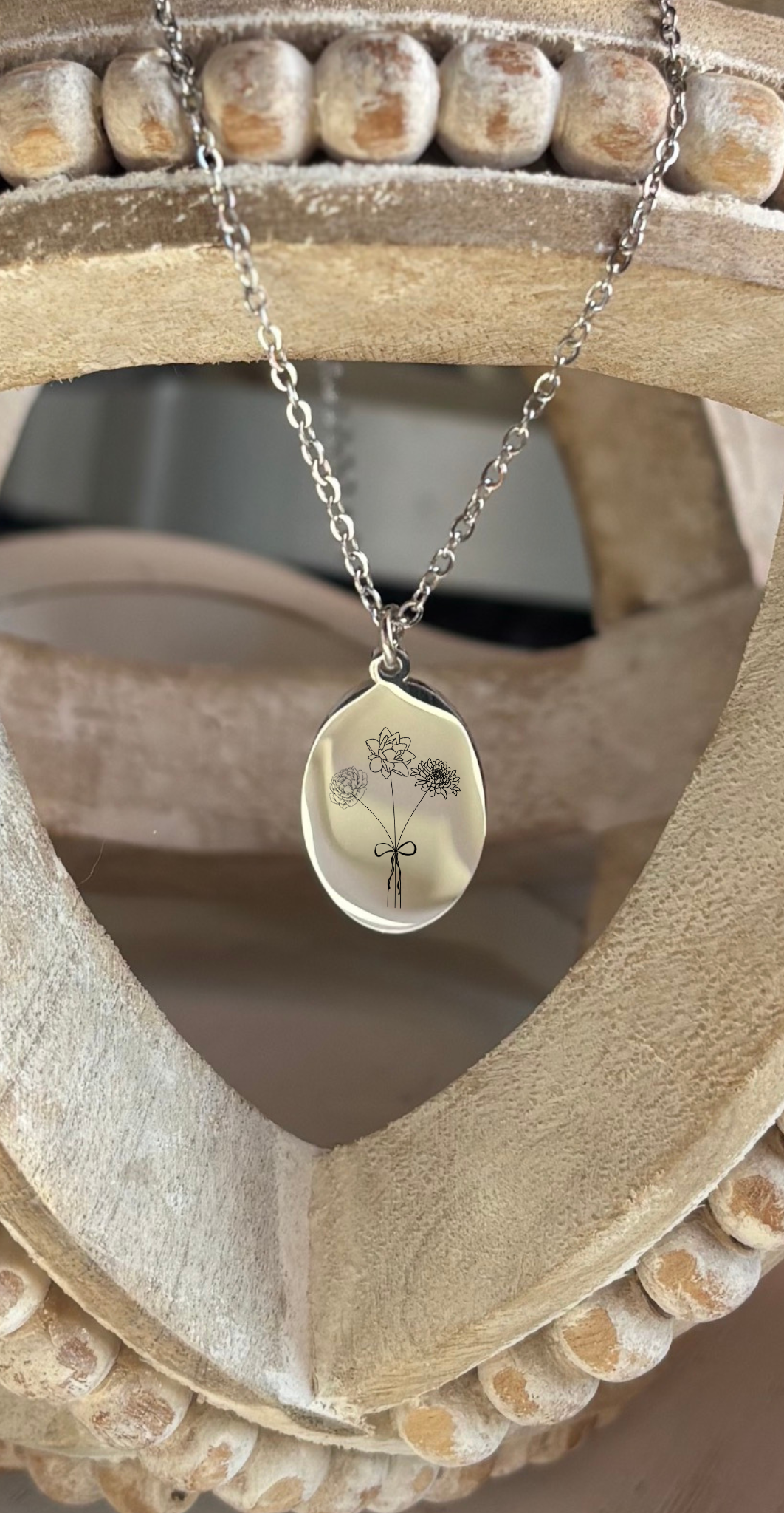 Silver necklace with a pendant featuring a floral design on a wooden stand.